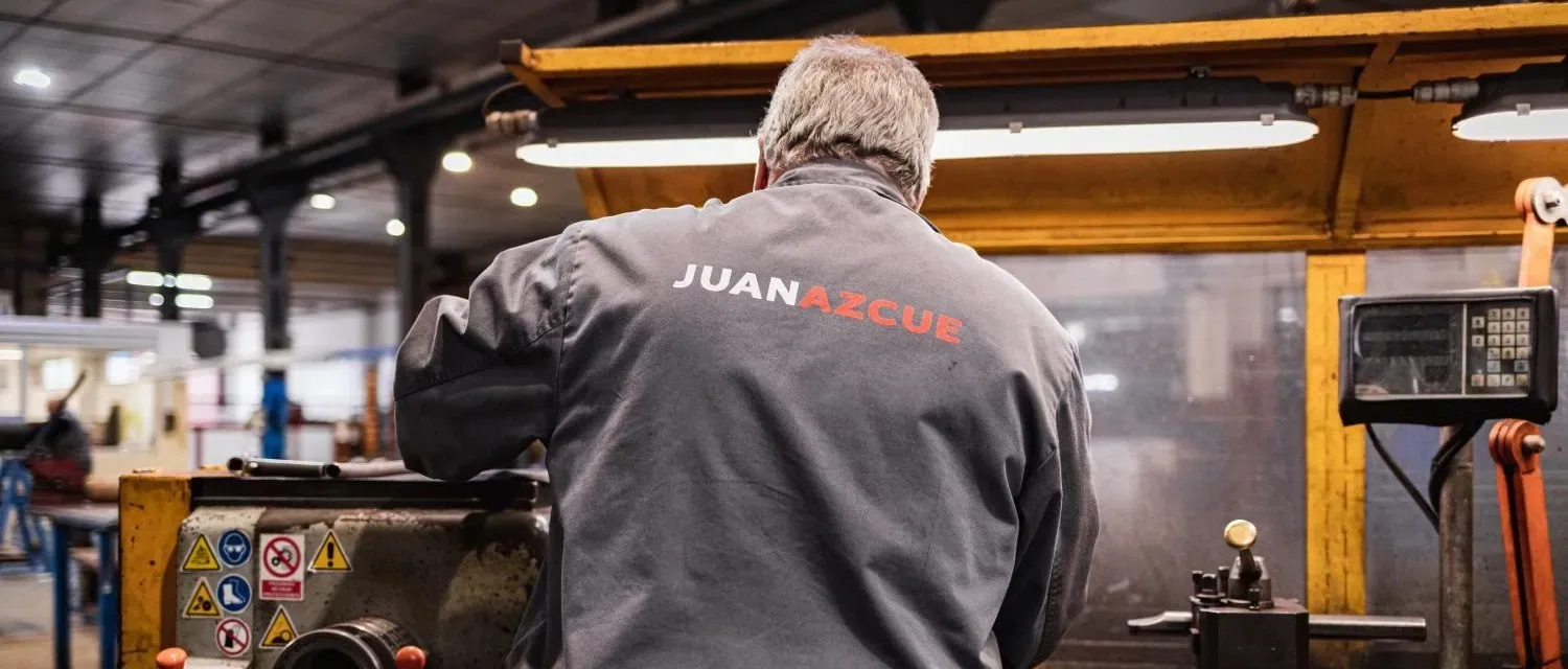 Operario del taller de Murcia trabajando en el torno, con el logotipo de Juan Azcue en la espalda