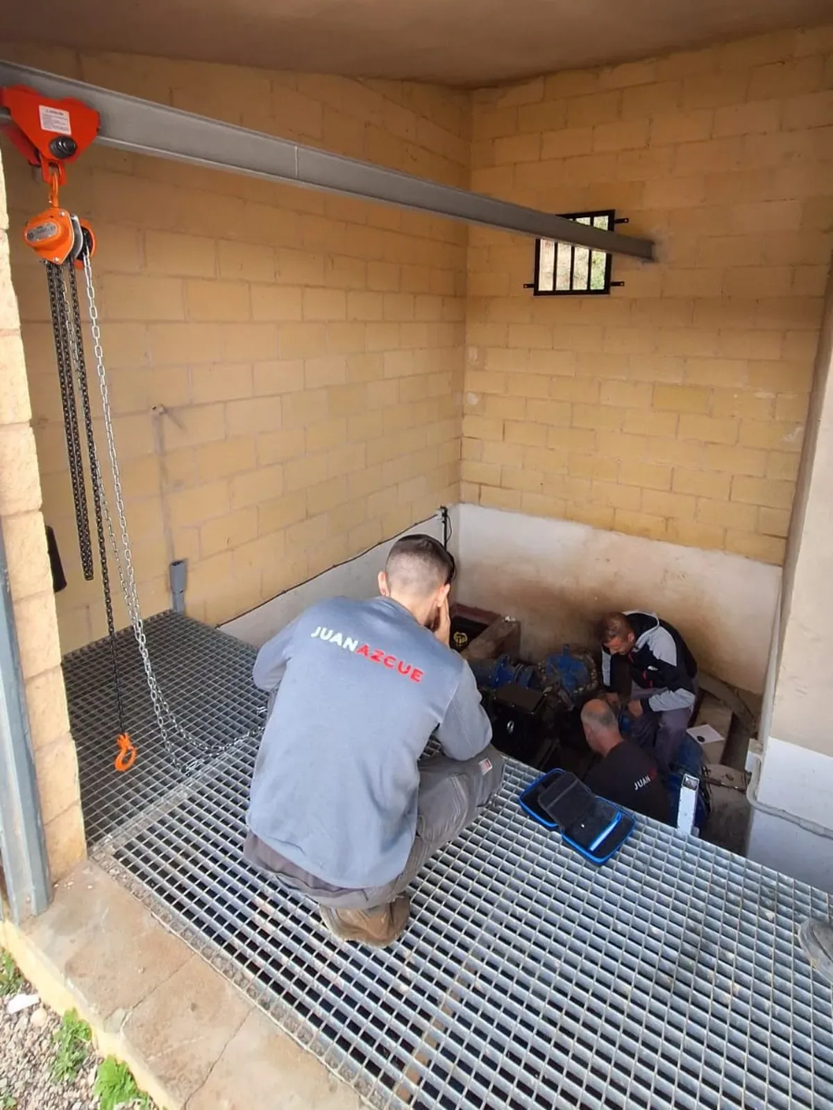 Tres operarios de Juan Azcue interviniendo sobre el equipo alojado en una cámara de bombeo enterrada, bajo el pórtico de la caseta